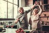 A senior couple dances in their kitchen while drinking wine and cooking dinner