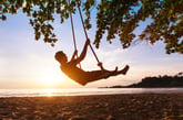 A man swings on a beach during sunset