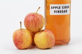 Apple cider vinegar next to a stack of apples