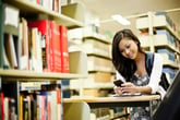 Woman student in library, looking at cellphone