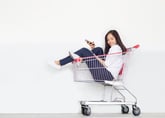 An Asian woman uses her phone while sitting in a shopping cart