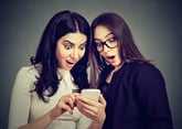 Two shocked looking women with cellphone