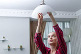A woman installs a light fixture in her home