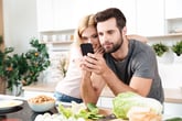 A couple looks for a recipe on a smartphone while cooking at home
