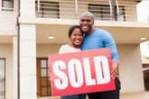 Couple holding a sold sign in front of a house