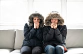 a couple wear parkas and shiver on their couch