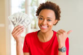 A young woman smiles while holding a fan of cash and giving the thumbs-up gesture