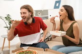Happy couple eating a pizza on a couch