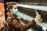 A woman in a surgical mask shops at a grocery store with empty shelves