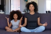 A mother and daughter meditating on a couch