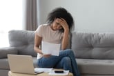 A stressed young woman worries about financial documents and bills over her laptop computer