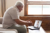 An older man talks to his doctor remotely on his laptop