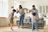 A happy family of parents and two children dancing in the living room
