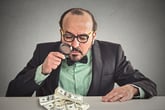 Businessman looking at cash with a magnifying glass