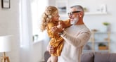 Grandfather or grandpa smiling and playing with granddaughter or grandchild in a bright happy home