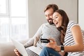 Happy couple using new credit card to shop online on laptop