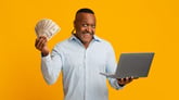 Excited man holding cash and a laptop computer