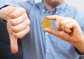 Man holding bitcoin and gesturing thumbs down in disapproval