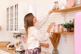 Smiling woman in the kitchen organizing her shelves and reaching for a jar of nuts