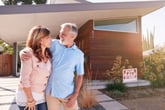 Older couple in front of a house for sale