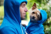 Man wearing a hoodie holding his pet dog in a cute matching hoodie outfit