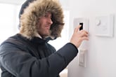 Man in winter coat setting thermostat