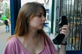 Confused woman looking at an antiquated payphone in a phone booth