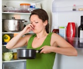 Disgusted woman holding rotten food in a pan that spoiled in the fridge