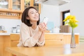 Happy woman using smartphone in kitchen and thinking