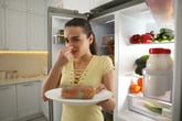 Upset woman holding her nose in disgust at spoiled food on a plate from the fridge