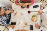 Restaurant diners eating food at the dining table after a meal with smartphones on the table