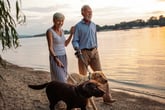 Senior couple walking their dogs on the lake beach
