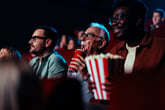 Senior man at the movie theater sipping a soda while viewers eat popcorn and watch with excitement
