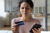 Woman looking at her phone skeptical or sad while holding credit card