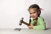 Grinning child holding a hammer ready to smash and destroy a smartphone