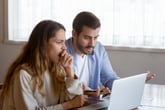 Couple perplexed by bills on laptop