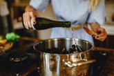 Woman adding white wine to a pan with mussels, preparing food