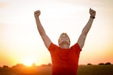 Excited man with arms high in the air celebrating victory or win at sunset outdoors