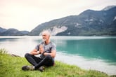 senior man meditating or doing yoga at a lake in the mountains in retirement