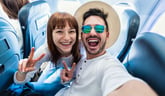 Happy excited couple in plane seats flying on vacation to have fun and showing peace sign gestures