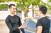 Smiling man taking car keys from used car seller after purchasing a used vehicle
