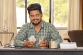 Happy man sitting in home office counting money saved