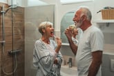 Senior couple brushing teeth in the bathroom together with walk-in shower and handheld showerhead