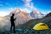 A man hiking in the wilderness with a tent stranded in the mountains uses his phone for an emergency SOS call