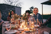 Smiling women at a dinner party outdoor table with wine glasses celebrating a winter holiday evening