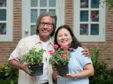 A couple holds flower pots in front of their home