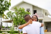 wife hugging her husband in front of the house they just move in while holding key