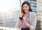 Excited smiling woman wearing glasses and looking at smartphone for happy news