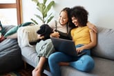 Couple using a laptop computer while sitting on the sofa with their dog