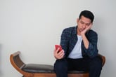 Tired, frustrated or bored man sitting with smartphone and waiting for a phone call possibly sitting on hold